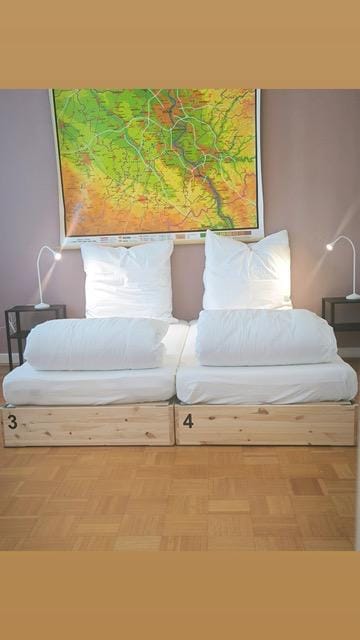 Zwei nummerierte Einzelbetten unter großer Landkarte im Emmas Hostel