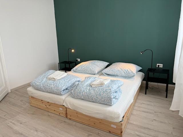Zwei Einzelbetten mit blau gemusterter Bettwäsche vor dunkelgrüner Wand im Emmas Hostel