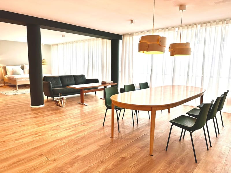 Ovaler Esstisch mit grünen Stühlen und offener Wohn- und Schlafzone in den Emmas Lofts